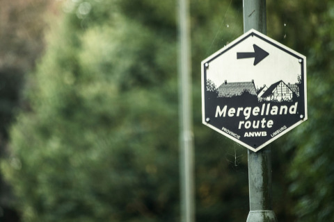Cartello del percorso Mergelland vicino a Meerssen, Limburgo, Paesi Bassi, con vegetazione sullo sfondo.