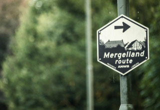 Cartello del percorso Mergelland vicino a Meerssen, Limburgo, Paesi Bassi, con vegetazione sullo sfondo.