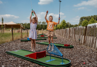 Two happy children play mini golf at Campsite 't Geuldal holiday park in Limburg, Netherlands, on a sunny day.