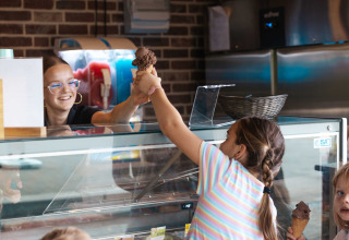 A smiling staff member serves ice cream to a child at the ice cream shop in Campsite 't Geuldal, Limburg.