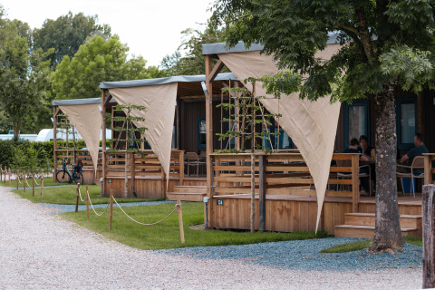 Wooden cabins with covered porches at Campsite 't Geuldal, a holiday park in Limburg, Netherlands, among trees.