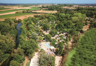 Vista aérea del camping Le Val de Cesse en Occitania, Francia, rodeado de campos verdes y un río cercano.