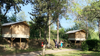 Due tende safari Bivouac Comfort rialzate in un campeggio alberato con ciclisti in primo piano.