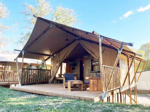 Alloggio glamping con struttura a tenda, terrazza in legno e area salotto all’aperto immersa nella natura.