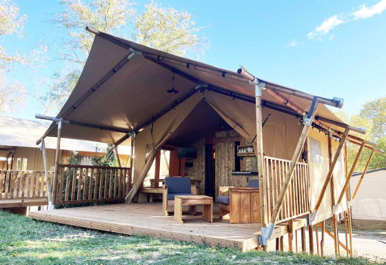 Alloggio glamping con struttura a tenda, terrazza in legno e area salotto all’aperto immersa nella natura.