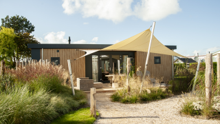 Een moderne Dune Lodge de Luxe bij Camping Zonneweelde in Nederland met zonnedoek en tuinpad.