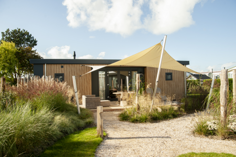 Een moderne Dune Lodge de Luxe bij Camping Zonneweelde in Nederland met zonnedoek en tuinpad.
