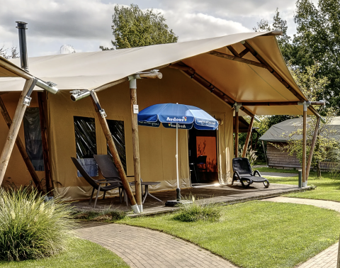 Photo extérieure d'une tente lodge safari de luxe avec terrasse, chaises longues et parasol sur camping