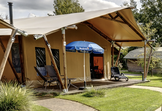 Außenaufnahme eines luxuriösen Safari-Zelt-Lodges mit Terrasse, Liegestühlen und Sonnenschirm auf Campingplatz