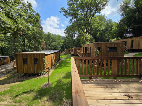 Holzhütten im Ferienpark Hameau de la Semois in Belgisch-Luxemburg, umgeben von grüner Natur und Bäumen.
