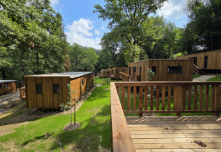 Wooden cabins at Hameau de la Semois holiday park in Belgian Luxembourg, surrounded by lush trees and nature.