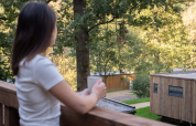 Donna con tazza sul balcone guarda cabine e alberi a Hameau de la Semois, Belgio.