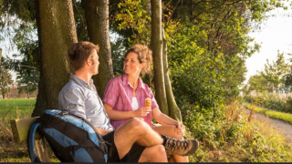 Dos personas descansan en un banco bajo los árboles en un sendero del Hameau de la Semois, Bélgica.