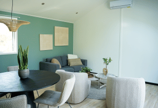 Sala moderna en Heuvelrug Cottage con pared verde, cómodas sillas, plantas y luz natural, Países Bajos.