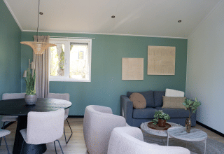 Moderne stue i Heuvelrug Cottage med grå sofa, runde borde, planter og spisebord på De Thijmse Berg.