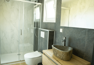 Baño moderno con lavabo de piedra y ducha de cristal en Heuvelrug Cottage, De Thijmse Berg, Países Bajos.
