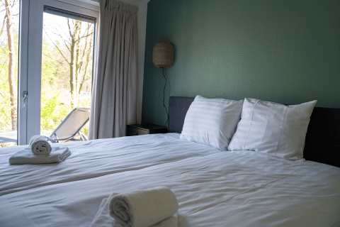 Gezellige slaapkamer in Heuvelrug Cottage, De Thijmse Berg, Nederland, met handdoeken en zicht op terras.