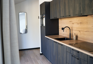 Modern kitchen with dark cabinets and wooden countertop at Heuvelrug Cottage, De Thijmse Berg, Netherlands.