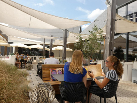 Terraza de restaurante en glamping con huéspedes disfrutando bajo toldos en un ambiente moderno y soleado.