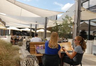 Terraza de restaurante en glamping con huéspedes disfrutando bajo toldos en un ambiente moderno y soleado.