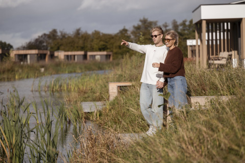 Deux personnes admirent la vue près de l’eau à Water lodge 2 + bain à remous, entourées de nature et de lodges.