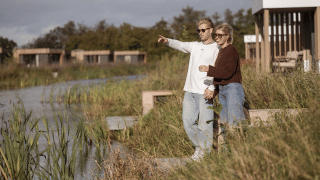 Deux personnes admirent la vue près de l’eau à Water lodge 2 + bain à remous, entourées de nature et de lodges.