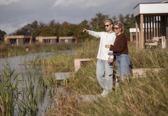 Two people enjoy the view by the water at Water lodge 2 + hot tub, surrounded by nature and modern lodges.