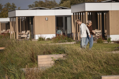 Dos personas caminan frente a cabañas modernas en Water lodge 2 + jacuzzi en Hofparken Wiltershaar, Países Bajos.