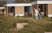 Dos personas caminan frente a cabañas modernas en Water lodge 2 + jacuzzi en Hofparken Wiltershaar, Países Bajos.