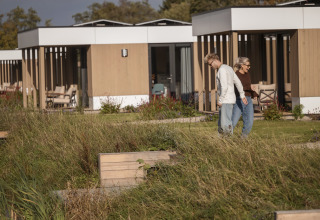 Deux personnes marchent devant des lodges modernes à Water lodge 2 + bain à remous à Hofparken Wiltershaar, Pays-Bas.