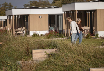 Deux personnes marchent devant des lodges modernes à Water lodge 2 + bain à remous à Hofparken Wiltershaar, Pays-Bas.