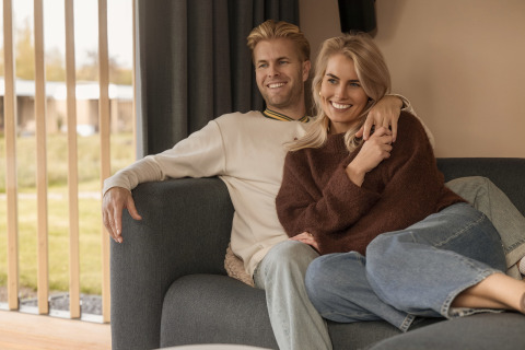 Glimlachend koppel ontspant samen op een zetel in Water lodge 2 + hot tub bij Hofparken Wiltershaar, Nederland.