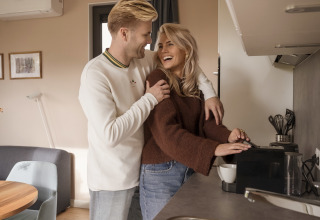 Young couple smiling and making coffee together in the kitchen at Water lodge 2 + hot tub in the Netherlands.