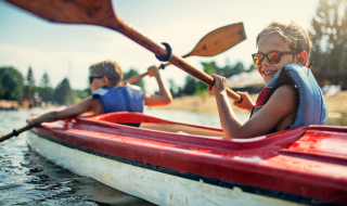 Dos niños reman juntos en un kayak rojo cerca de Bouillon, Bélgica Luxemburgo, en un día soleado.