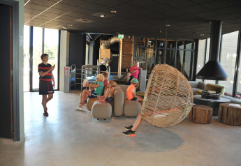 Bambini si rilassano e giocano nel moderno lounge di Zonneweelde Lodge Deluxe al Camping Zonneweelde, Paesi Bassi.