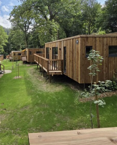 Houten chalets in vakantiepark Hameau de la Semois, Belgisch Luxemburg, omringd door groene natuur.