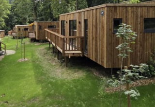 Houten chalets in vakantiepark Hameau de la Semois, Belgisch Luxemburg, omringd door groene natuur.