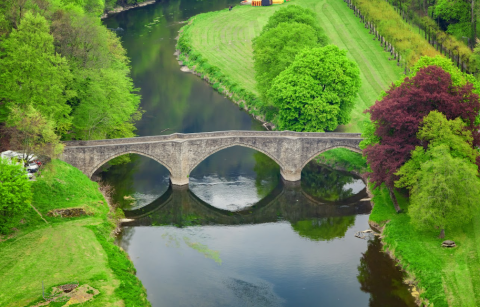 Ponte di pietra sul fiume tra verde lussureggiante nel parco vacanze Hameau de la Semois, Belgio Lussemburgo.
