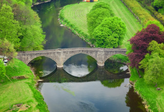 Steinbrücke über einen Fluss von üppigem Grün im Hameau de la Semois Ferienpark, Belgien Luxemburg.