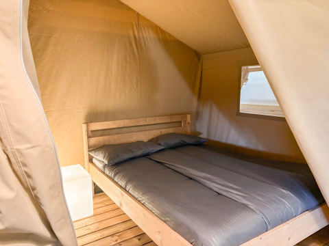 Interieur van safaritent met tweepersoonsbed en nachtkastje bij Vestbirk Camping in Denemarken.