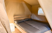 Interieur van safaritent met tweepersoonsbed en nachtkastje bij Vestbirk Camping in Denemarken.