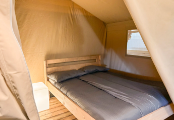 Interior de tienda safari con cama doble y mesita de noche en Vestbirk Camping, Dinamarca.