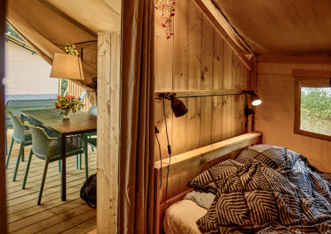 Indvendig visning af en komfortabel safaritelte med seng, bord og stole på Vestbirk Camping, Danmark.
