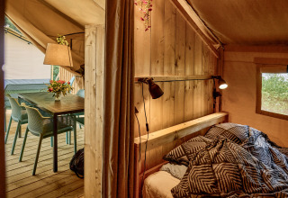 Indvendig visning af en komfortabel safaritelte med seng, bord og stole på Vestbirk Camping, Danmark.