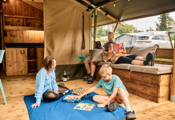 Famille détendue dans une tente safari avec sanitaires privés à Vestbirk Camping, enfants jouent au sol.