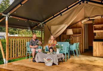 Pareja relajándose en una tienda safari con instalaciones sanitarias en Vestbirk Camping, Dinamarca.