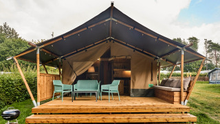 Tienda safari con instalaciones sanitarias, terraza con sillas y sofá, rodeada de vegetación y árboles.