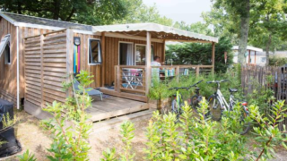 Premium wooden mobile home at Flower Camping La Canadienne in France, featuring terrace and bicycles.