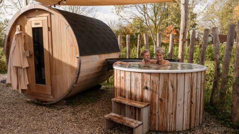 Koppel ontspant in een hottub en sauna buiten bij Water lodge 6 Deluxe, omgeven door houten hek.