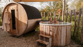 Couple relaxing in outdoor hot tub and sauna at Water lodge 6 Deluxe, surrounded by wooden fencing.